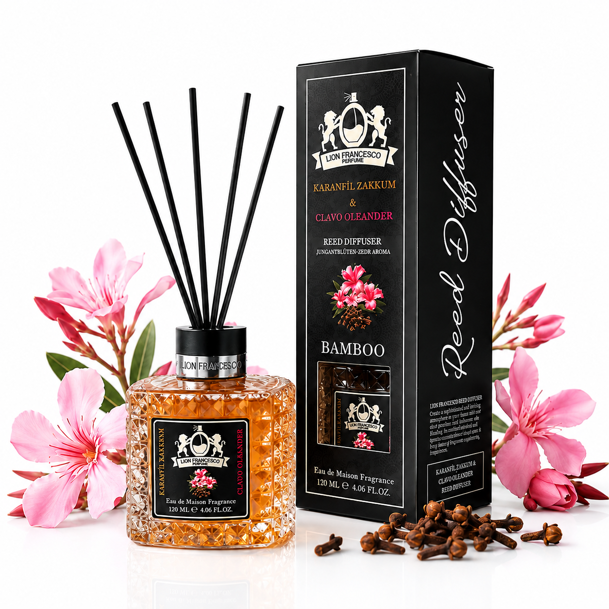 A reed diffuser bottle with amber-colored liquid and white beads, black reeds, and a black label, shown next to its black retail box. Pink flowers and cloves are styled around the product on a white background.