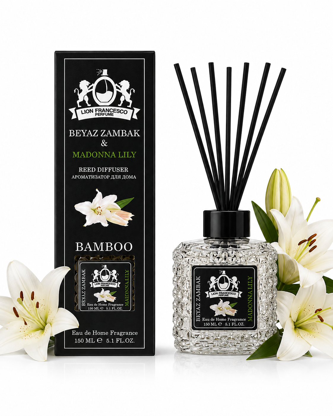 A reed diffuser bottle with black reeds and a black label, shown beside its matching black box. White lilies and green leaves are placed around the product on a clean white background.