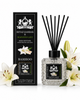 A reed diffuser bottle with black reeds and a black label, shown beside its matching black box. White lilies and green leaves are placed around the product on a clean white background.