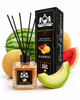 A reed diffuser bottle with black reeds and a black label, shown next to its black branded box. The scene is styled with melon slices and watermelon wedges on a white background.
